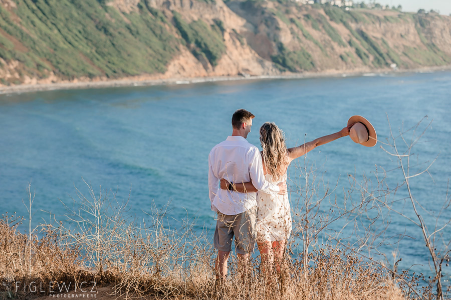 couple looking off palos verdes cliff to ocean tossing hat